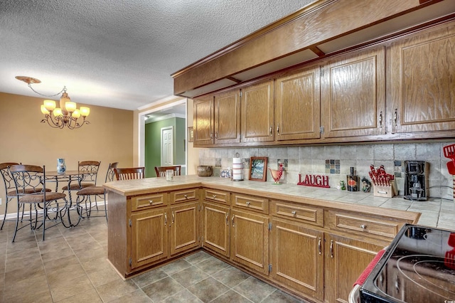 kitchen featuring backsplash, tile counters, a peninsula, an inviting chandelier, and electric range