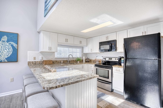 kitchen with a sink, black appliances, white cabinets, a kitchen breakfast bar, and light wood-type flooring