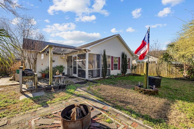 rear view of property with fence, an outdoor fire pit, a lawn, a sunroom, and a patio