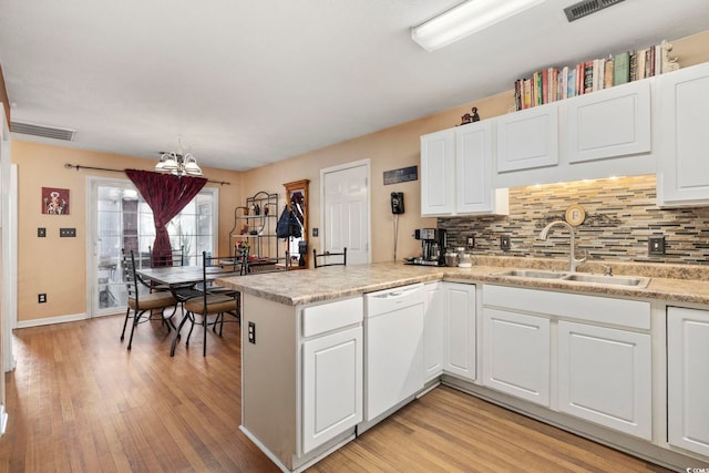 kitchen featuring visible vents, a peninsula, white dishwasher, a sink, and light wood-type flooring