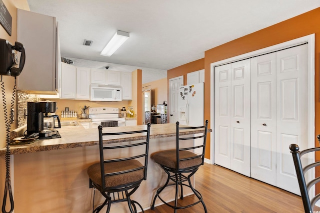 kitchen featuring white appliances, visible vents, a peninsula, light wood-style flooring, and white cabinets