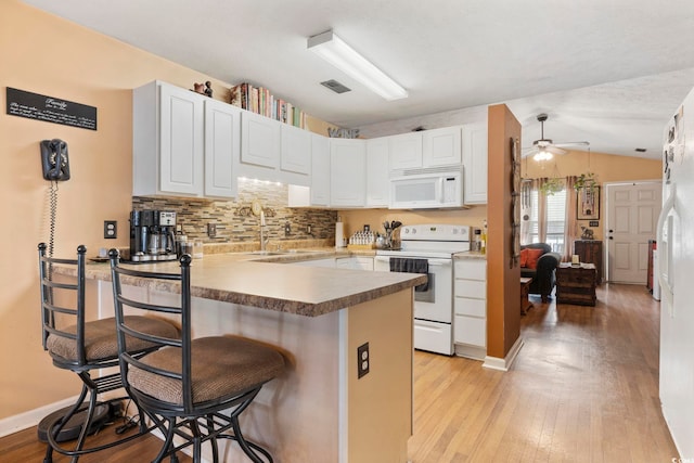 kitchen featuring white appliances, light wood-style flooring, a peninsula, and a sink