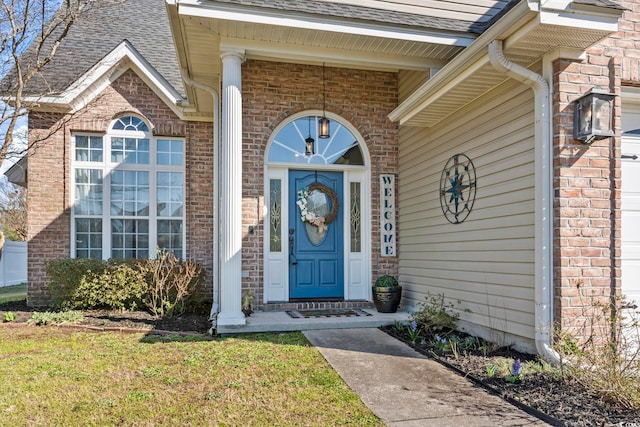 entrance to property with brick siding, a garage, and roof with shingles