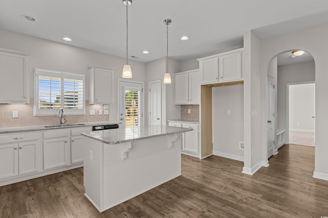 kitchen featuring a center island, dark wood finished floors, arched walkways, white cabinets, and a sink