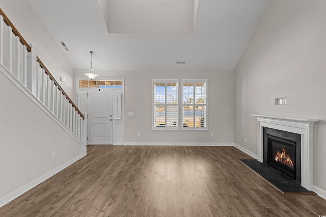 unfurnished living room featuring dark wood finished floors, a glass covered fireplace, stairway, and baseboards