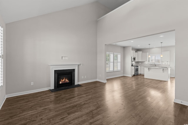 unfurnished living room with dark wood-type flooring, high vaulted ceiling, a glass covered fireplace, recessed lighting, and baseboards