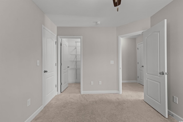 unfurnished bedroom with a ceiling fan, baseboards, a spacious closet, a closet, and light colored carpet