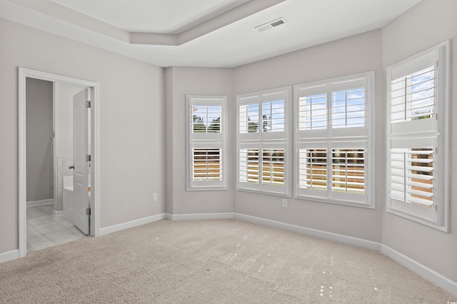 carpeted spare room featuring a tray ceiling, visible vents, and baseboards