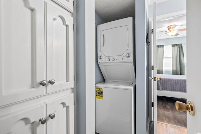 laundry area with stacked washer and clothes dryer, a textured ceiling, wood finished floors, ceiling fan, and laundry area