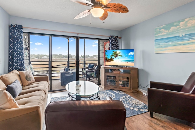 living area with ceiling fan, baseboards, a textured ceiling, and wood finished floors