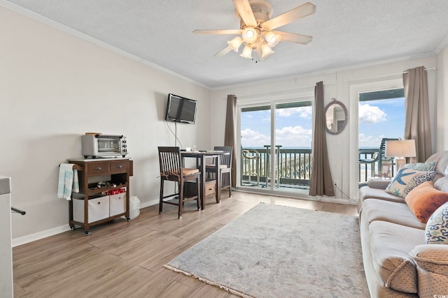 living area with ornamental molding, a ceiling fan, a textured ceiling, wood finished floors, and baseboards