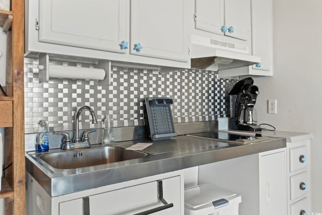 kitchen with stainless steel countertops, backsplash, under cabinet range hood, and white cabinetry