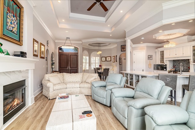 living room with a raised ceiling, arched walkways, a high end fireplace, and light wood finished floors