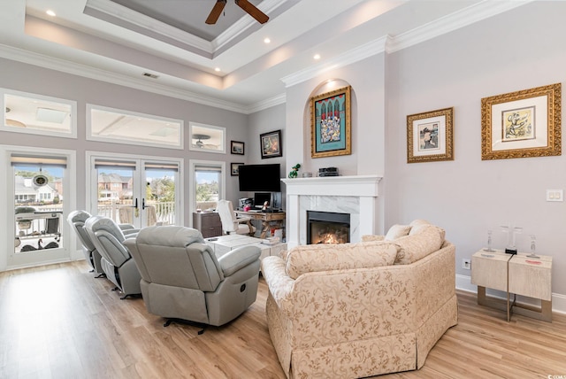 living room with baseboards, light wood finished floors, a premium fireplace, a tray ceiling, and crown molding