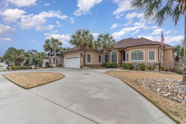 view of front of home with stucco siding, stone siding, a garage, and driveway