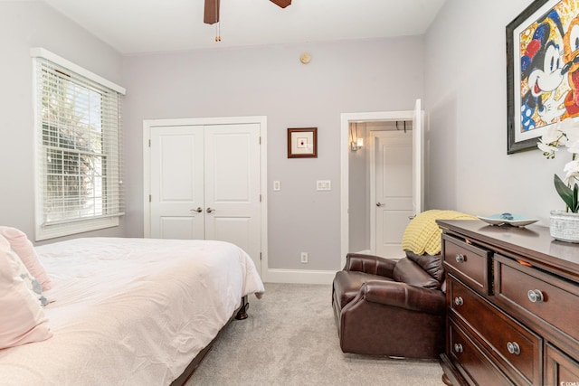 bedroom with a closet, baseboards, light colored carpet, and ceiling fan