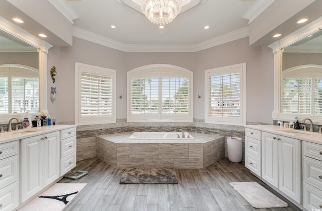 bathroom featuring ornamental molding, two vanities, a garden tub, and a sink