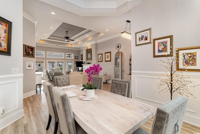 dining area with arched walkways, ornamental molding, light wood-style floors, wainscoting, and a raised ceiling