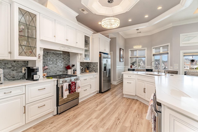 kitchen featuring stainless steel appliances, light wood-style floors, white cabinetry, a raised ceiling, and a sink