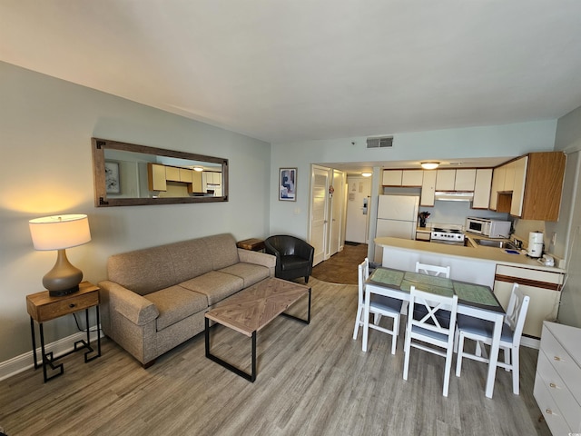 living room with light wood-style floors, visible vents, and baseboards