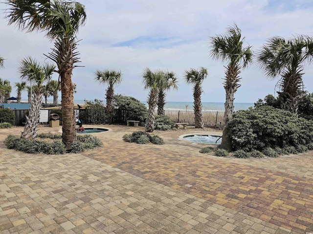 view of patio / terrace with a community hot tub, a community pool, fence, and a water view