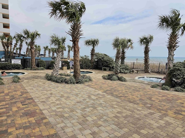 view of patio with a water view, a community hot tub, and fence