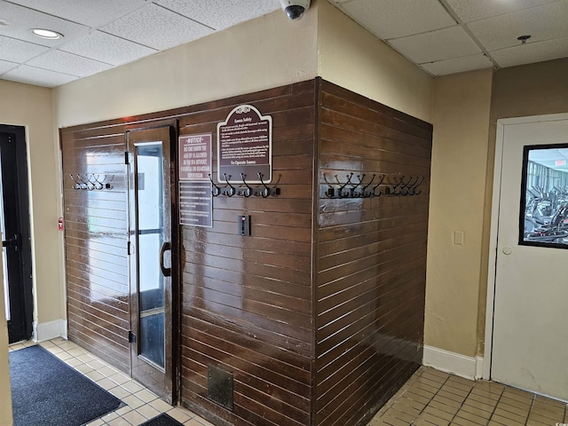 doorway featuring tile patterned floors, a drop ceiling, and baseboards