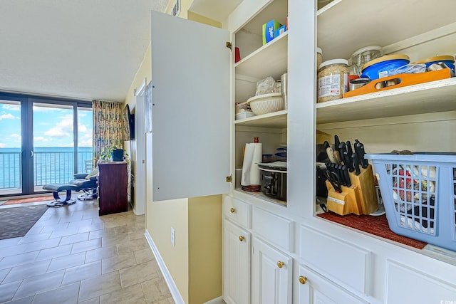 interior space with a wall of windows, baseboards, white cabinets, and light tile patterned floors