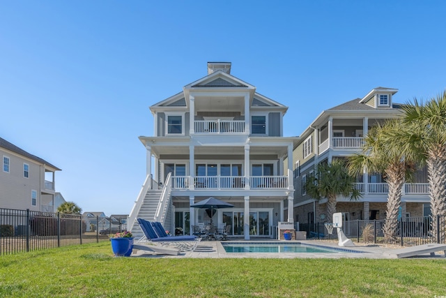 rear view of property featuring stairway, a fenced in pool, fence, a patio area, and a lawn