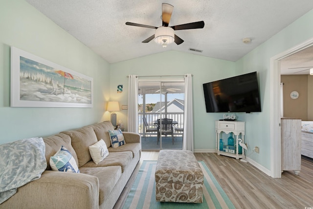 living area with wood finished floors, visible vents, ceiling fan, vaulted ceiling, and a textured ceiling