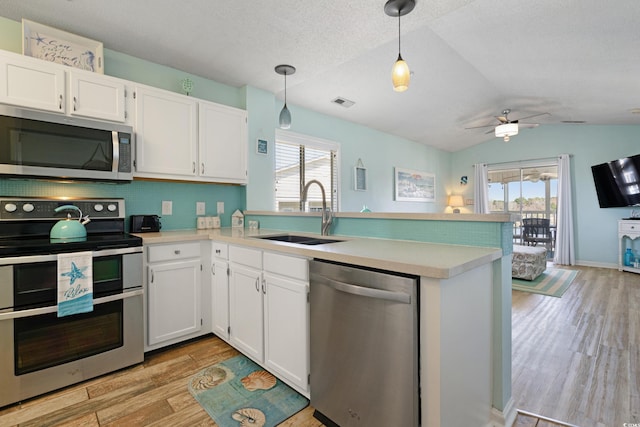 kitchen with light wood finished floors, light countertops, a peninsula, stainless steel appliances, and a sink