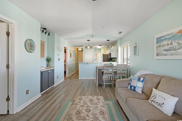 living room with vaulted ceiling, light wood-style flooring, baseboards, and visible vents