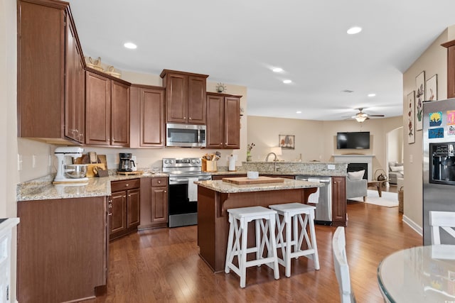 kitchen featuring a kitchen breakfast bar, stainless steel appliances, a peninsula, a fireplace, and ceiling fan