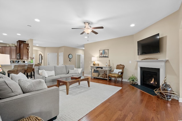 living area with wood finished floors, a ceiling fan, baseboards, a fireplace with flush hearth, and recessed lighting