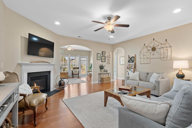 living room featuring a fireplace with flush hearth, light wood-style flooring, recessed lighting, arched walkways, and ceiling fan