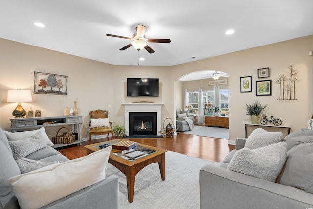 living area with a fireplace with flush hearth, wood finished floors, and a ceiling fan