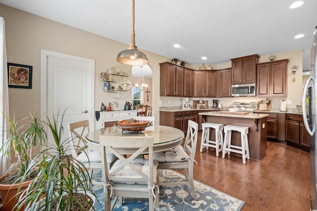 kitchen featuring wood finished floors, a kitchen island, arched walkways, appliances with stainless steel finishes, and a kitchen breakfast bar