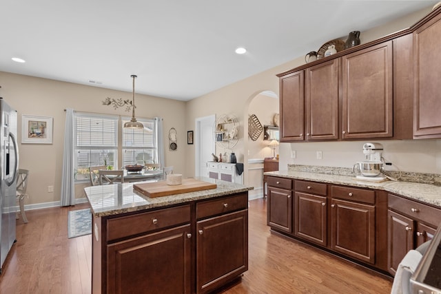 kitchen with stainless steel fridge, light stone counters, light wood-type flooring, and a center island