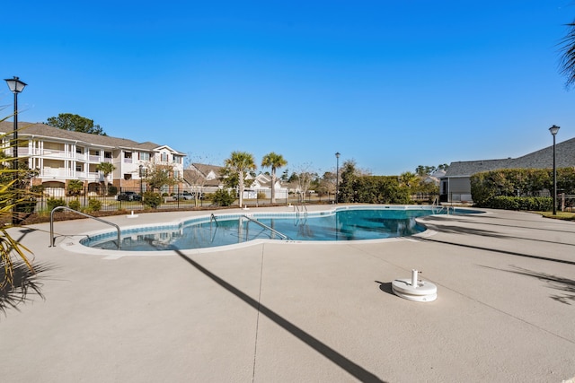 pool with a patio, fence, and a residential view