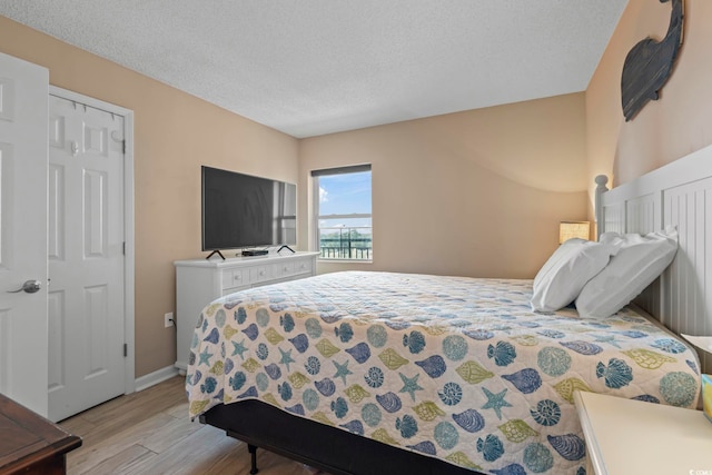 bedroom featuring baseboards, light wood-style floors, and a textured ceiling