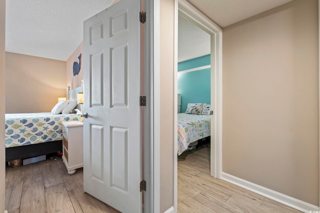 hall featuring baseboards, a textured ceiling, and light wood finished floors