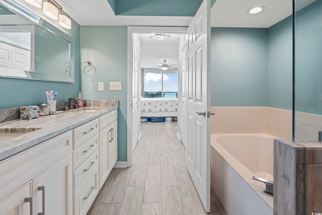 ensuite bathroom featuring connected bathroom, wood finish floors, a garden tub, double vanity, and a sink