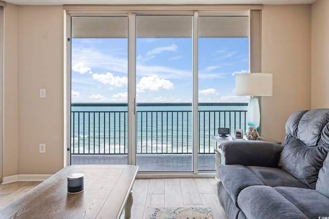 living room featuring expansive windows, baseboards, light wood-style floors, and a water view