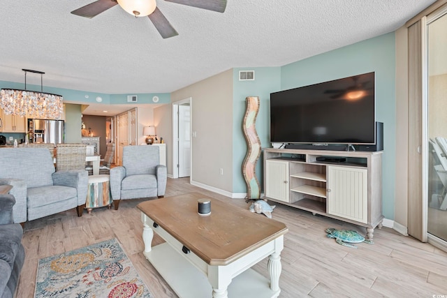 living room featuring a textured ceiling, visible vents, light wood finished floors, and ceiling fan