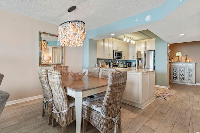 dining space with a textured ceiling, light wood-style flooring, baseboards, and a chandelier