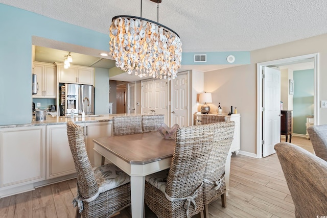 dining area featuring a notable chandelier, light wood-style floors, visible vents, and a textured ceiling