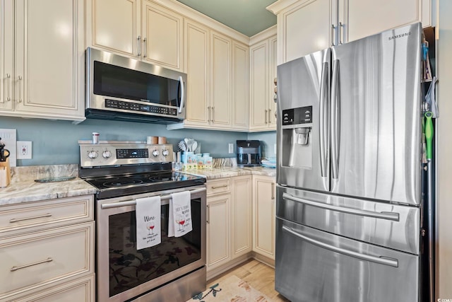 kitchen featuring light stone counters, light wood finished floors, appliances with stainless steel finishes, and cream cabinets