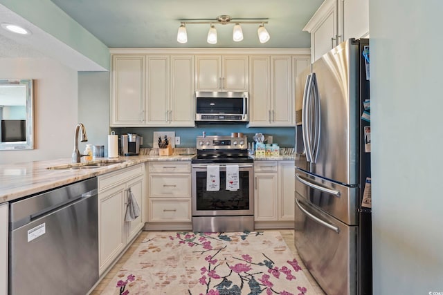 kitchen featuring a sink, stainless steel appliances, light stone counters, and cream cabinets