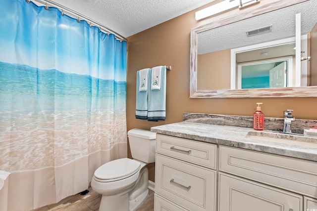 bathroom featuring visible vents, toilet, a textured ceiling, wood finished floors, and vanity