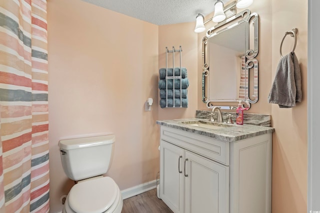 bathroom featuring baseboards, toilet, vanity, wood finished floors, and a textured ceiling